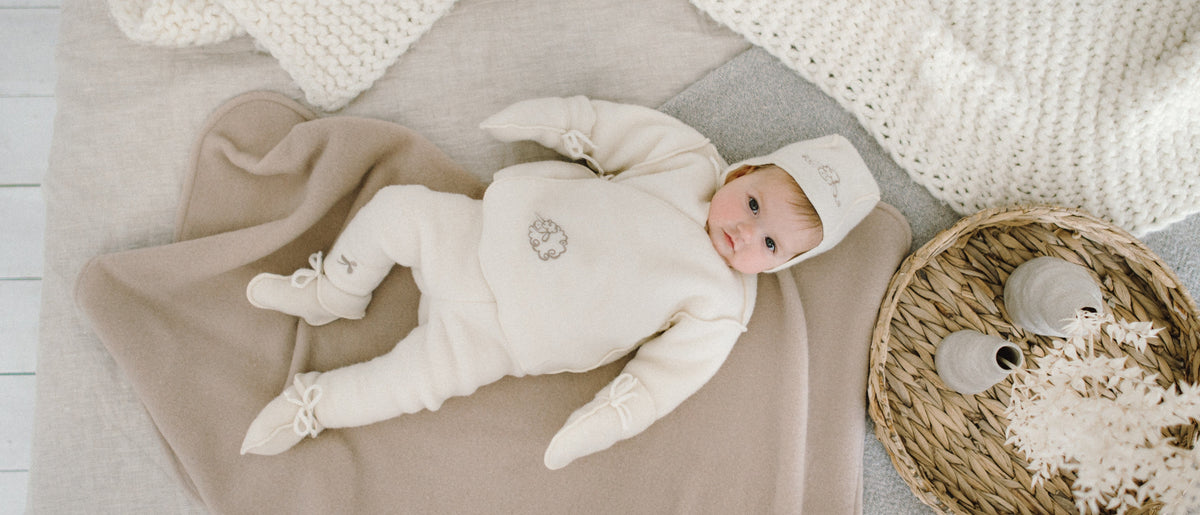 Baby in een merino boxpakje met mutsje en slofjes op een zachte deken
